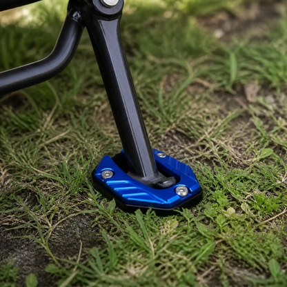 Blue CNC kickstand pad supporting a motorcycle side stand on grass
